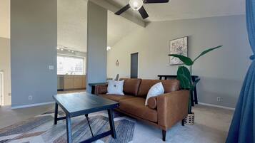Relax in this stylish living room with a comfortable sofa, coffee table, and ceiling fan. Enjoy the view from the large window and kitchen beyond.