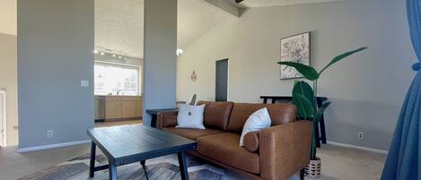 A living room with a brown leather sofa, a dark wooden coffee table, a ceiling fan, and a large green plant.