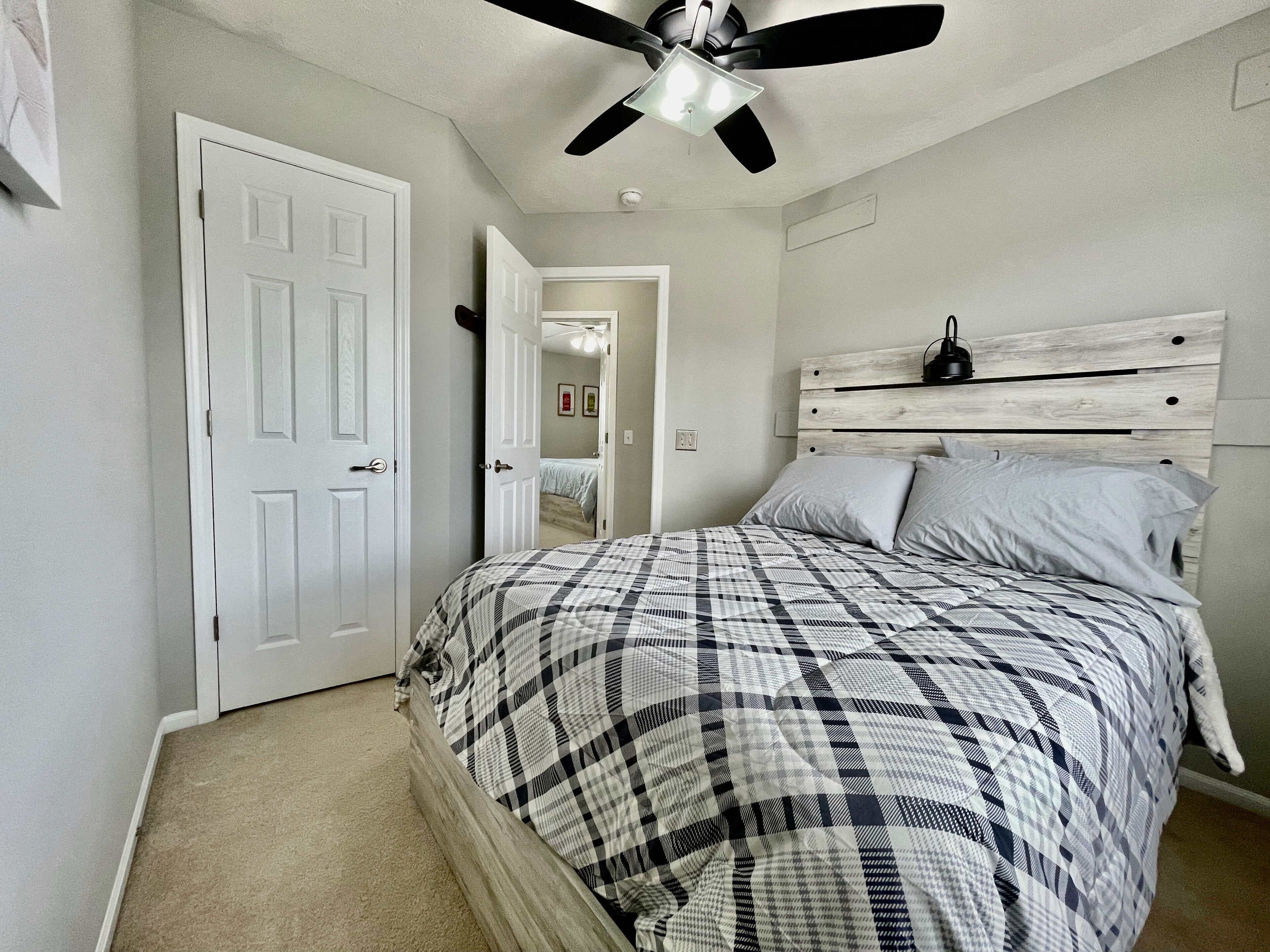 A bedroom with a bed, a ceiling fan, a white door, and a light switch on the wall.