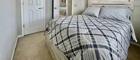 A bedroom with a bed, a ceiling fan, a white door, and a light switch on the wall.