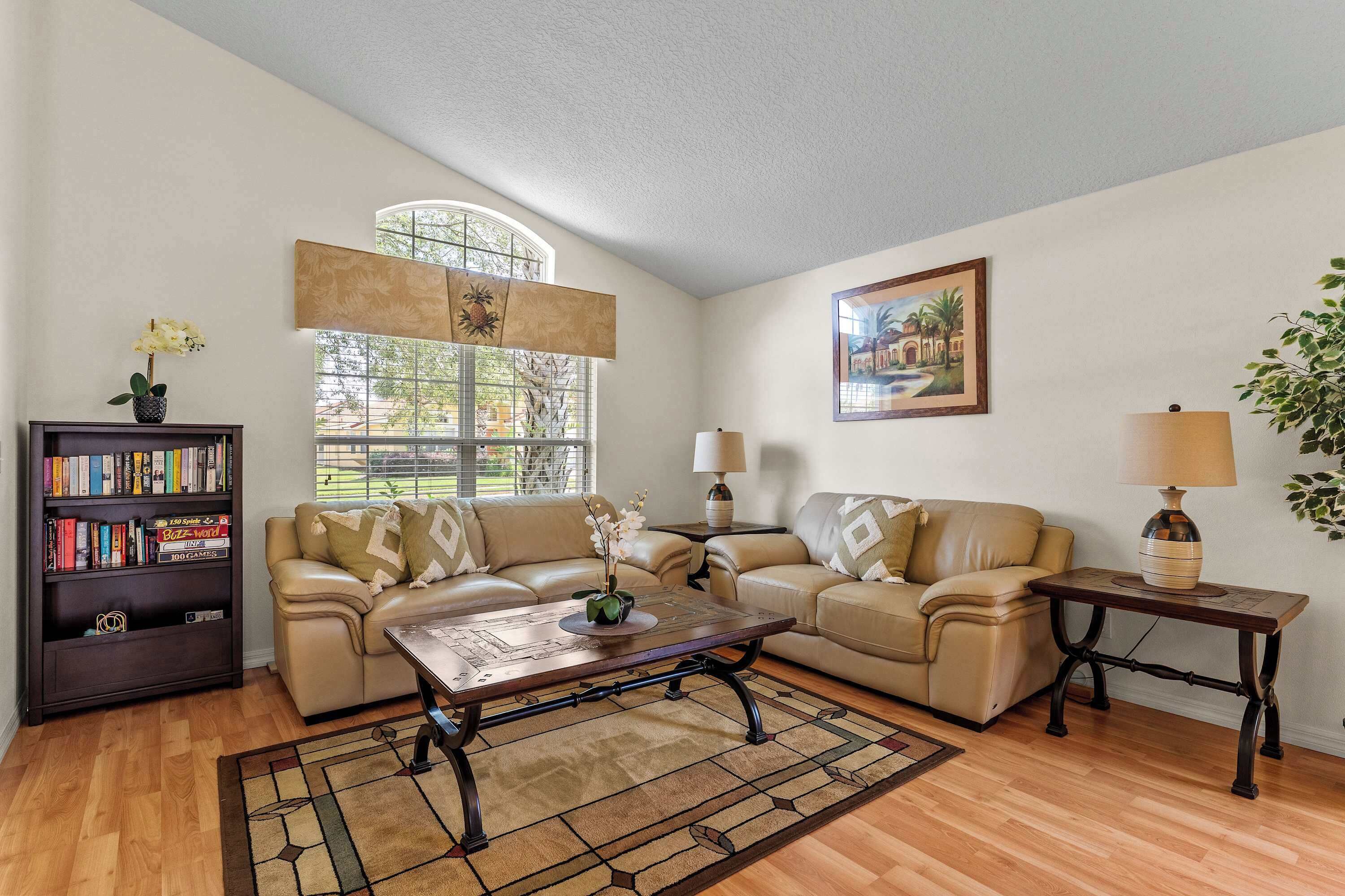 A living room with a sofa, coffee table, and lamps. There is a bookshelf with books and a potted plant.
