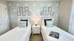 A twin room with two beds, a nightstand with a lamp, and a wall with cloud-themed artwork.