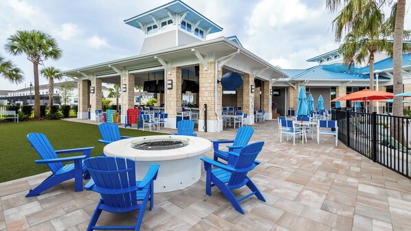 An outdoor patio with blue Adirondack chairs, a fire pit, and umbrellas.