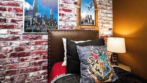 A room with a brick wall, a poster of Hogwarts, a framed picture of a castle, a red pillow, a black pillow with a crest, and a lamp. - A Little Galaxy Far Far Away (Davenport)