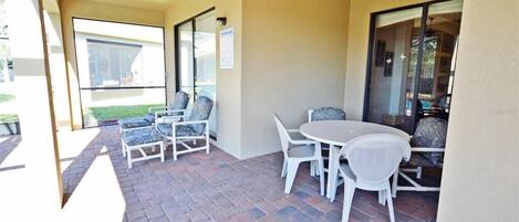An outdoor patio with a ceiling fan, white wicker furniture, and a brick floor.