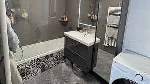 A modern bathroom with a bathtub, a sink, a mirror, and a washing machine.