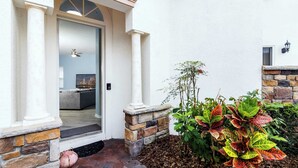 Een moderne entree met een glazen deur, een stenen muur en een plantenbak met kleurrijke beplanting.
