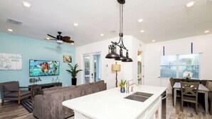 A modern kitchen with a central island, a dining area with a table and chairs, a living room with a sofa, and a ceiling fan. - Trade Winds Life - Margaritaville (Kissimmee)
