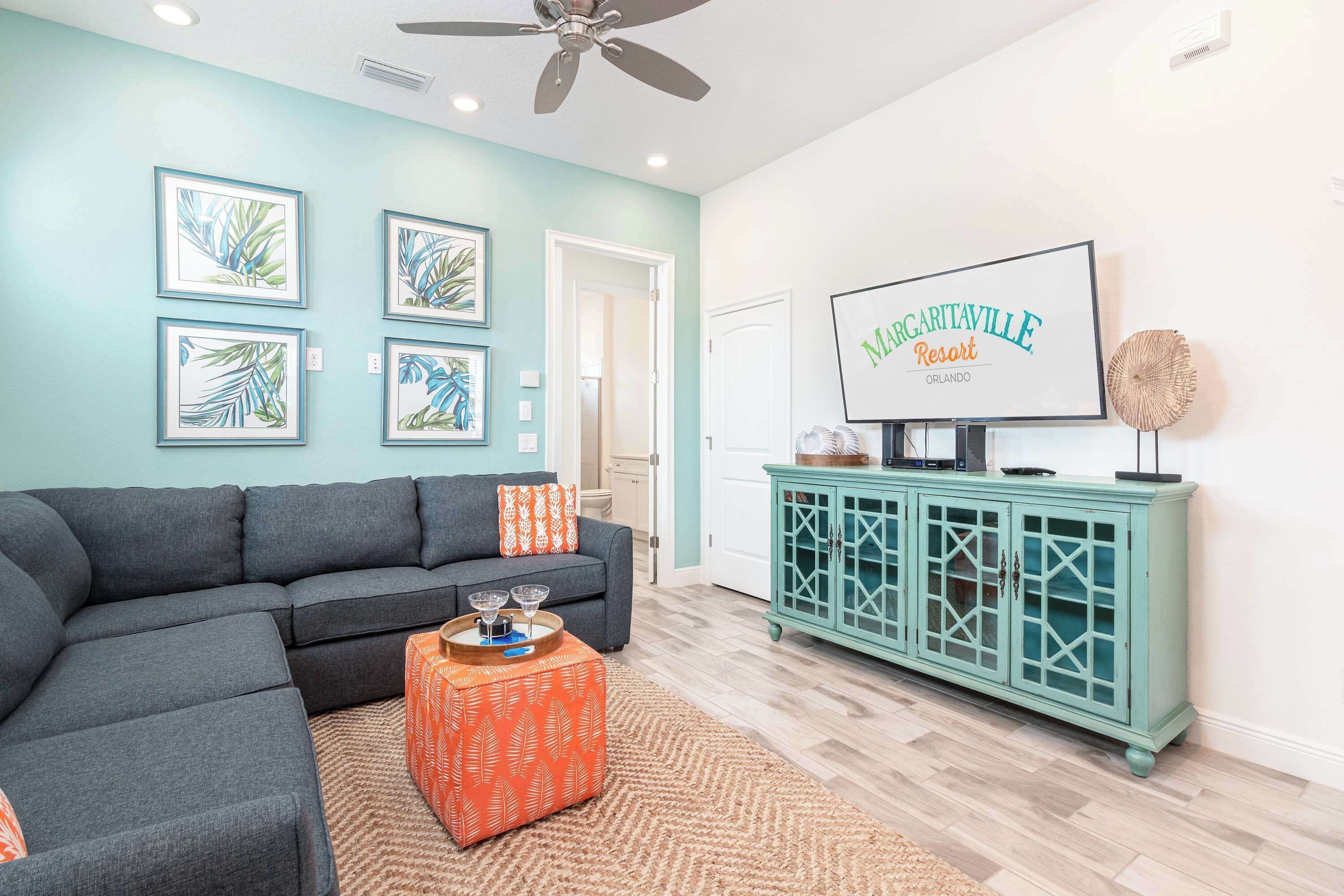 A living room with a teal wall, a gray sectional sofa, a teal cabinet, and framed artwork.