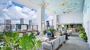 Un vaste salon sur le toit, doté de mobilier moderne, de grandes fenêtres offrant une vue sur la ville et d’un plafond agrémenté de motifs artistiques.