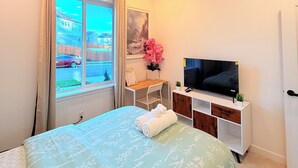 Ett hotellrum med en säng, ett skrivbord med en stol, en tv och ett fönster med gardiner.
