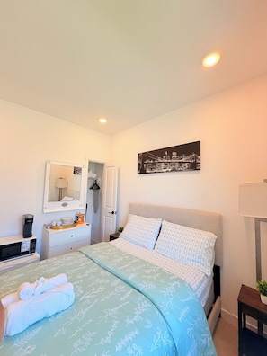 A hotel room with a bed, a bedside table with a lamp, a mirror, a painting on the wall, and a small plant. - Cozy Private Room 1 Near Seattle & Mt. Rainier – Quiet & Comfy Stay + Car Rental (Bonney Lake)