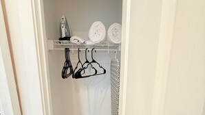 En smal hall med en vit dörr på vänster sida, en vit vägg och en liten hylla med hoprullade handdukar och en hårtork.