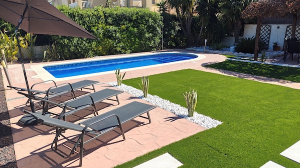 A swimming pool with lounge chairs, a patio area, and a well-maintained lawn.