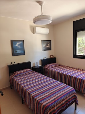 A bedroom with two beds, a ceiling fan, a window, and two framed pictures on the wall.