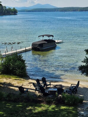 A lakeside setting with a boat docked at a pier, surrounded by chairs and a table on the shore.