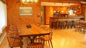 A wooden-paneled dining room with a long table and chairs, a kitchen with wooden cabinets and a central island, and a chandelier.