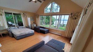 A spacious bedroom with a large bed, a sofa, and a view of a lake through large windows.