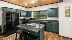 A modern kitchen with dark green cabinets, a black refrigerator, and a granite countertop.