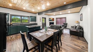 A modern kitchen with dark green cabinets, a wooden dining table, and a fireplace.