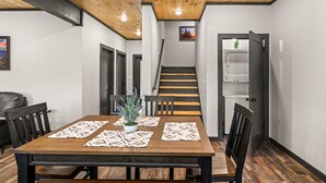 A dining area with a wooden table and chairs, a potted plant, and a view of a staircase leading to a laundry room.