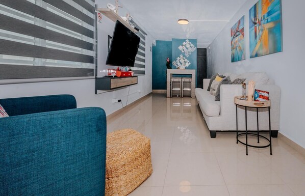 A modern living room with a flat-screen TV, a sofa, a coffee table, and abstract wall art. - Charming 2-bedroom apartment in enchanting Cataño with AC, WiFi (Cataño)