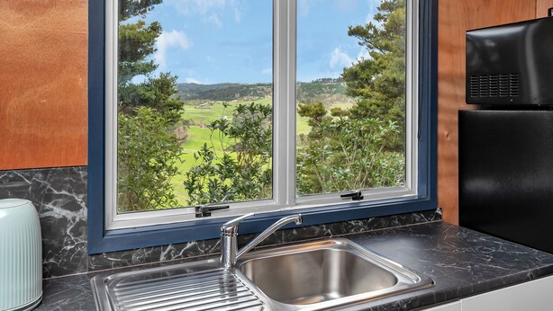 Una cocina con un amplio ventanal, un lavamanos de acero inoxidable y un refrigerador negro.