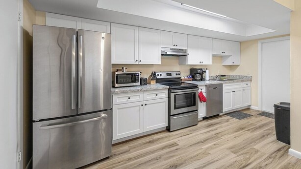 A modern kitchen with stainless steel appliances, white cabinetry, and a wood floor. - Clean & Cozy 2, Near MLB Airport, HRMC, Food, Nightlife, Beaches & Shopping! (Melbourne)