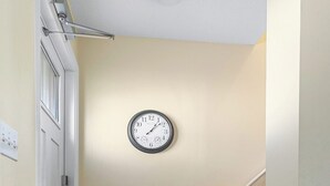 A hallway with a wooden floor, a red and beige doormat, a wall clock, and a white door. - Clean & Cozy 2, Near MLB Airport, HRMC, Food, Nightlife, Beaches & Shopping! (Melbourne)