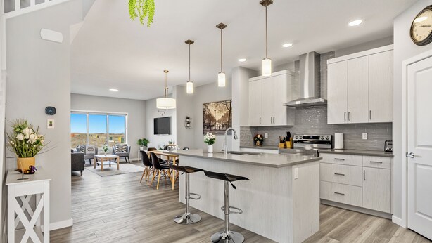 A modern kitchen with a central island, bar stools, and pendant lighting. - Cozy 3 Bedroom Home in Rangeview (Calgary)