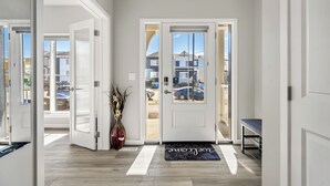 A clean, modern entrance with a welcome mat, a vase with dried plants, and a bench. - Cozy 3 Bedroom Home in Rangeview (Calgary)