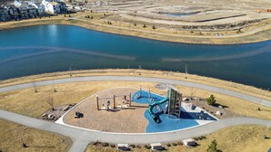 An aerial view of a park with a playground, a lake, and surrounding residential buildings. - Cozy 3 Bedroom Home in Rangeview (Calgary)