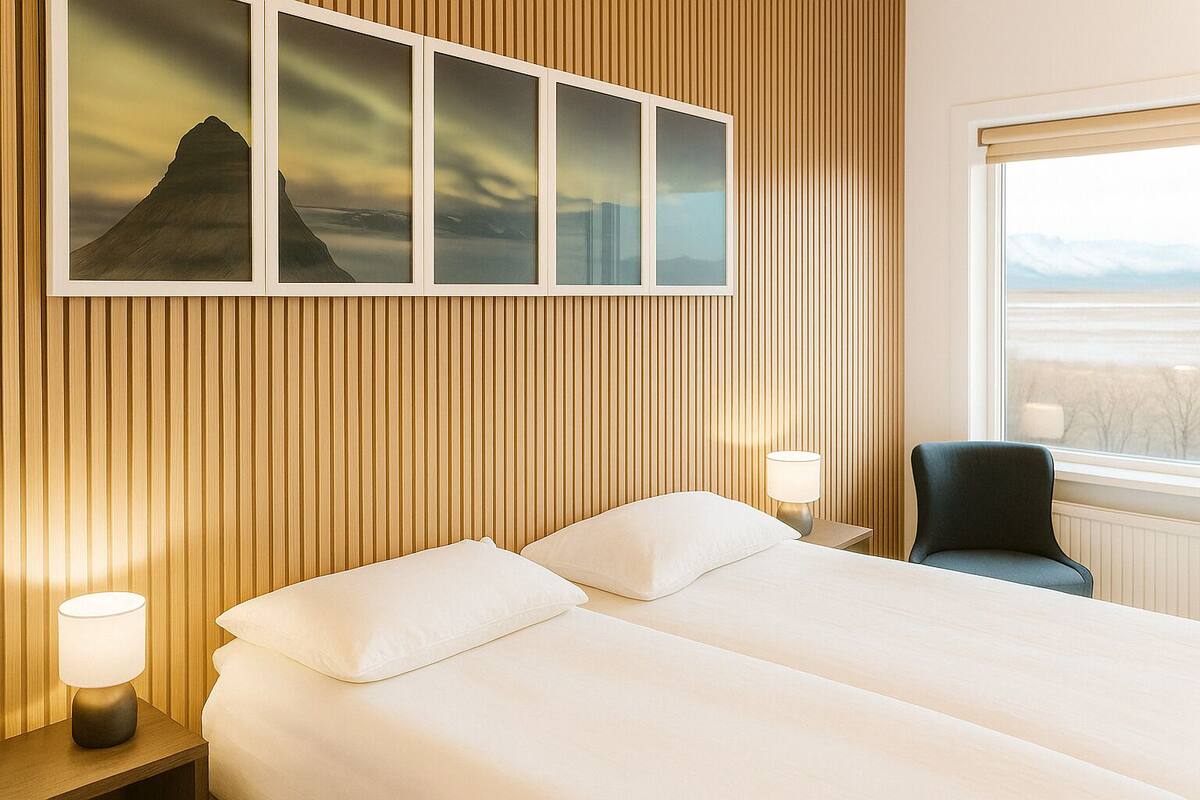 Ein Hotelzimmer mit Bett, zwei Nachttischlampen, einem Sessel und einem Fenster mit Blick auf eine Landschaft.