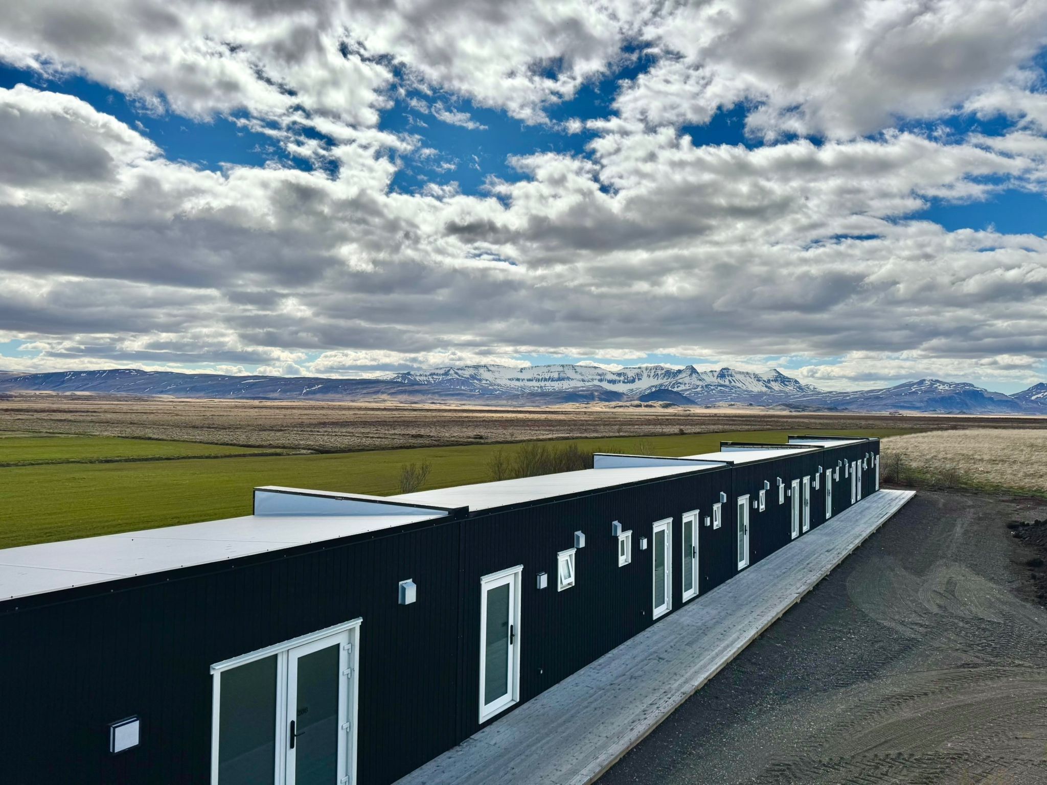 Una hilera de edificios negros con ventanas blancas, sobre un fondo de paisaje montañoso bajo un cielo nublado.