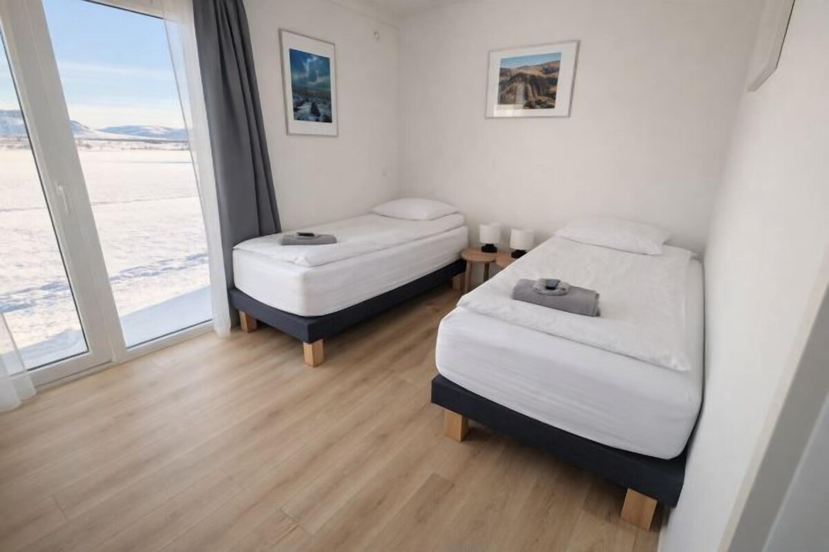 A room with two beds, a wooden floor, and a large window with a view of a snowy landscape.