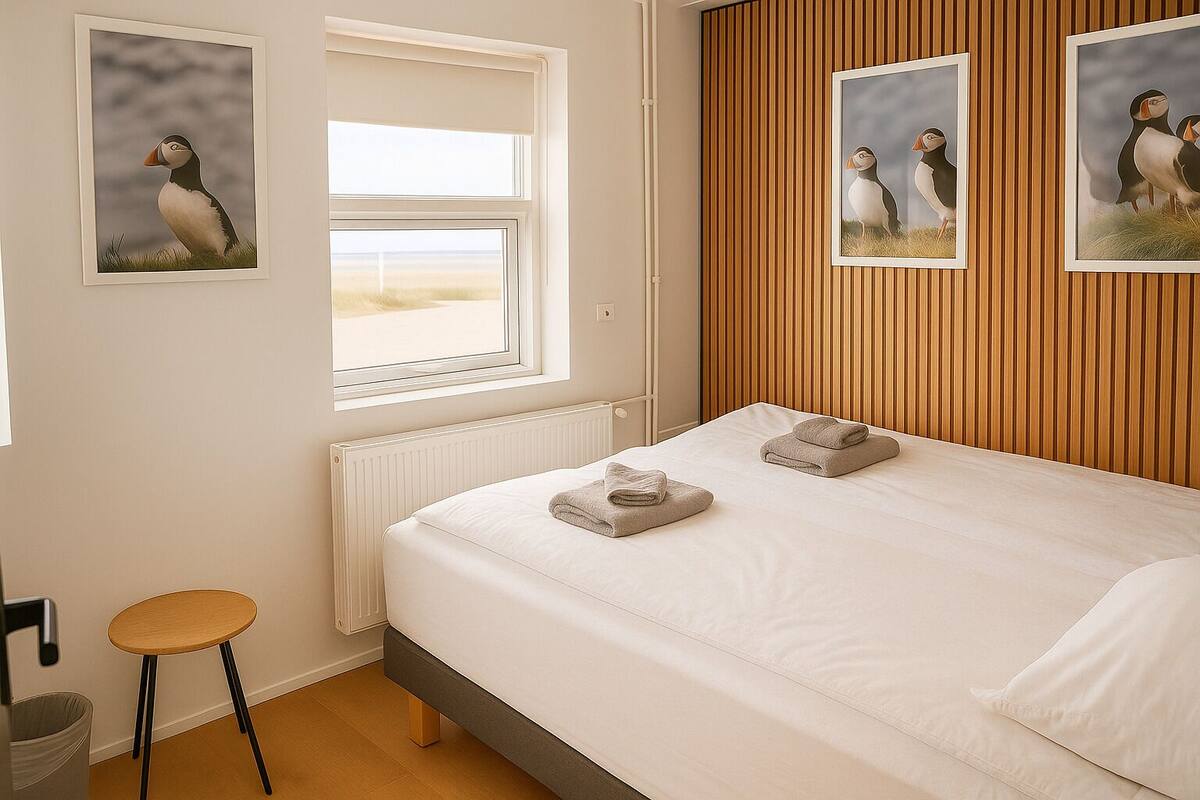 Ein Schlafzimmer mit Bett, zwei Handtüchern, einem Fenster, einer Heizung, einer Holzvertäfelung und einem Puffin-Bild.