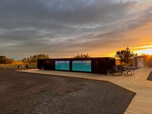 A modern outdoor seating area with a wooden deck, two large screens, and a small building with a door. - The Hvítá Inn (Borgarbyggd)