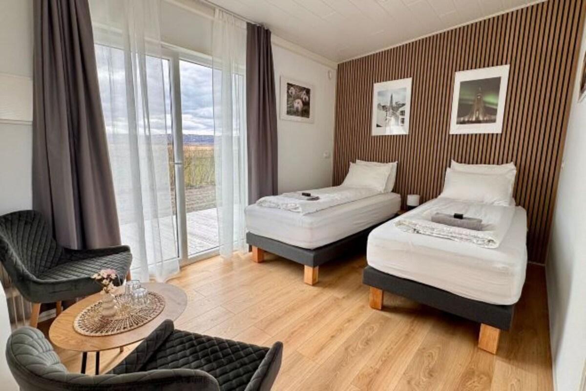 Habitació d'hotel moderna amb dos llits, una zona de seients i vista a l'exterior.