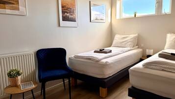Un dormitorio con dos camas, una silla, un radiador y cuadros enmarcados en la pared.