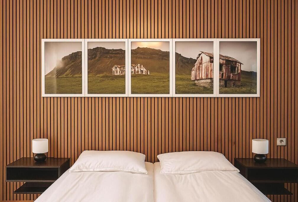 A room with a bed, two bedside tables, and a wall-mounted picture of a rural landscape.