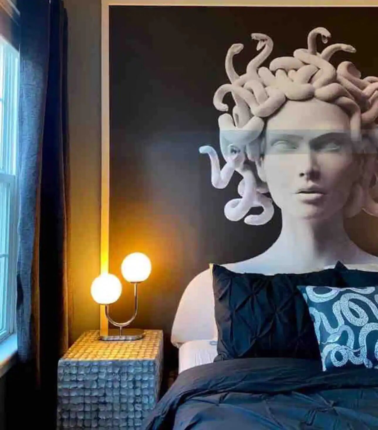 Une pièce comprenant un lit, une lampe fix ée au mur et une grande sculpture abstraite.