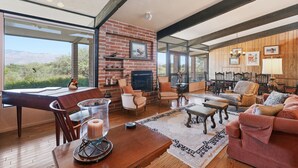 A spacious living room with a brick fireplace, large windows, and a cozy seating area. - Lazy P Ranch 12-acre retreat, spectacular mountain views, bring your horses! (Tucson)
