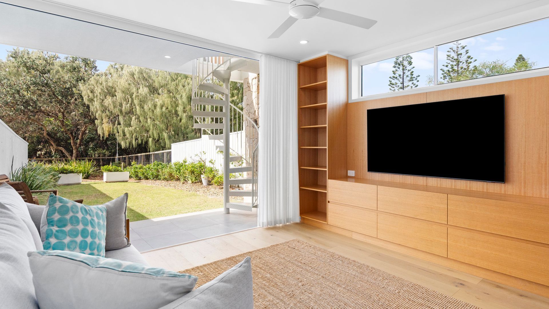 A modern living room with a large TV, a staircase leading to a balcony, and a view of the outdoors.