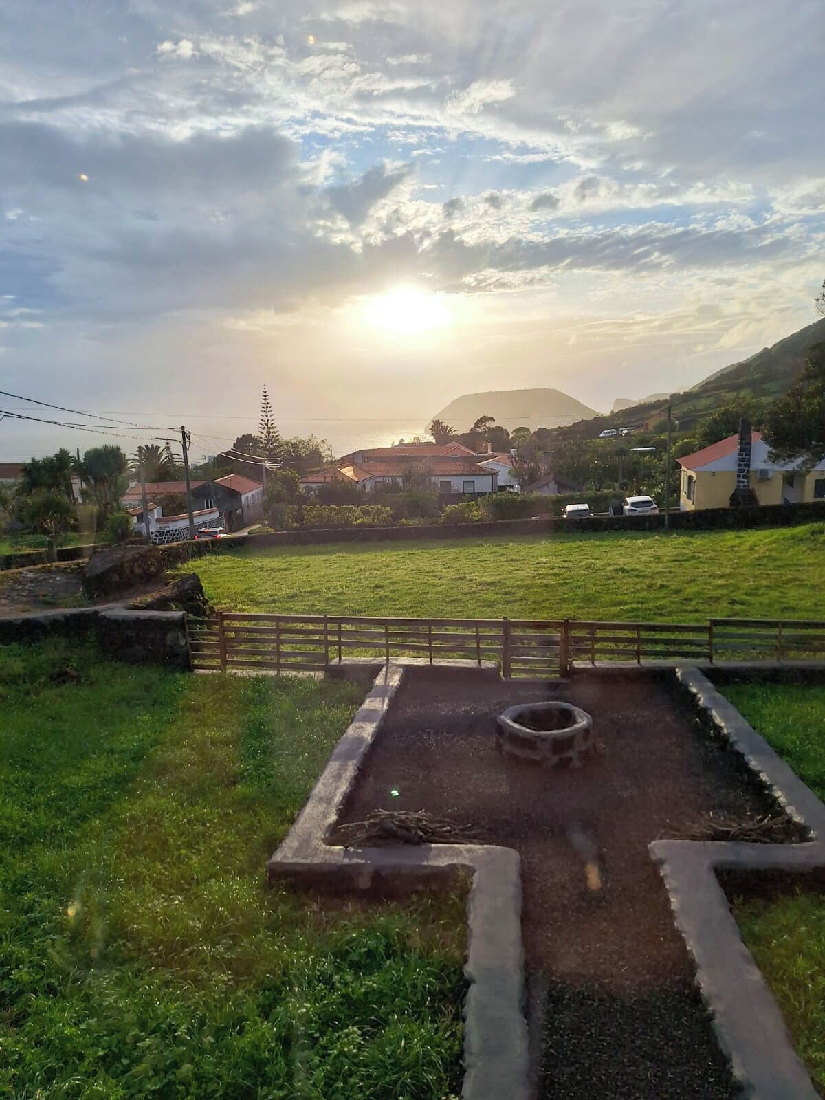 Paisaje rural con un campo cubierto de hierba, una valla de madera y algunas casas al fondo.