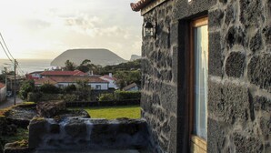 A stone building with a tiled roof, a wooden door, and a view of a mountain and ocean in the background.