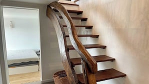 A wooden staircase with a unique design, leading to a bedroom with a bed and a nightstand.