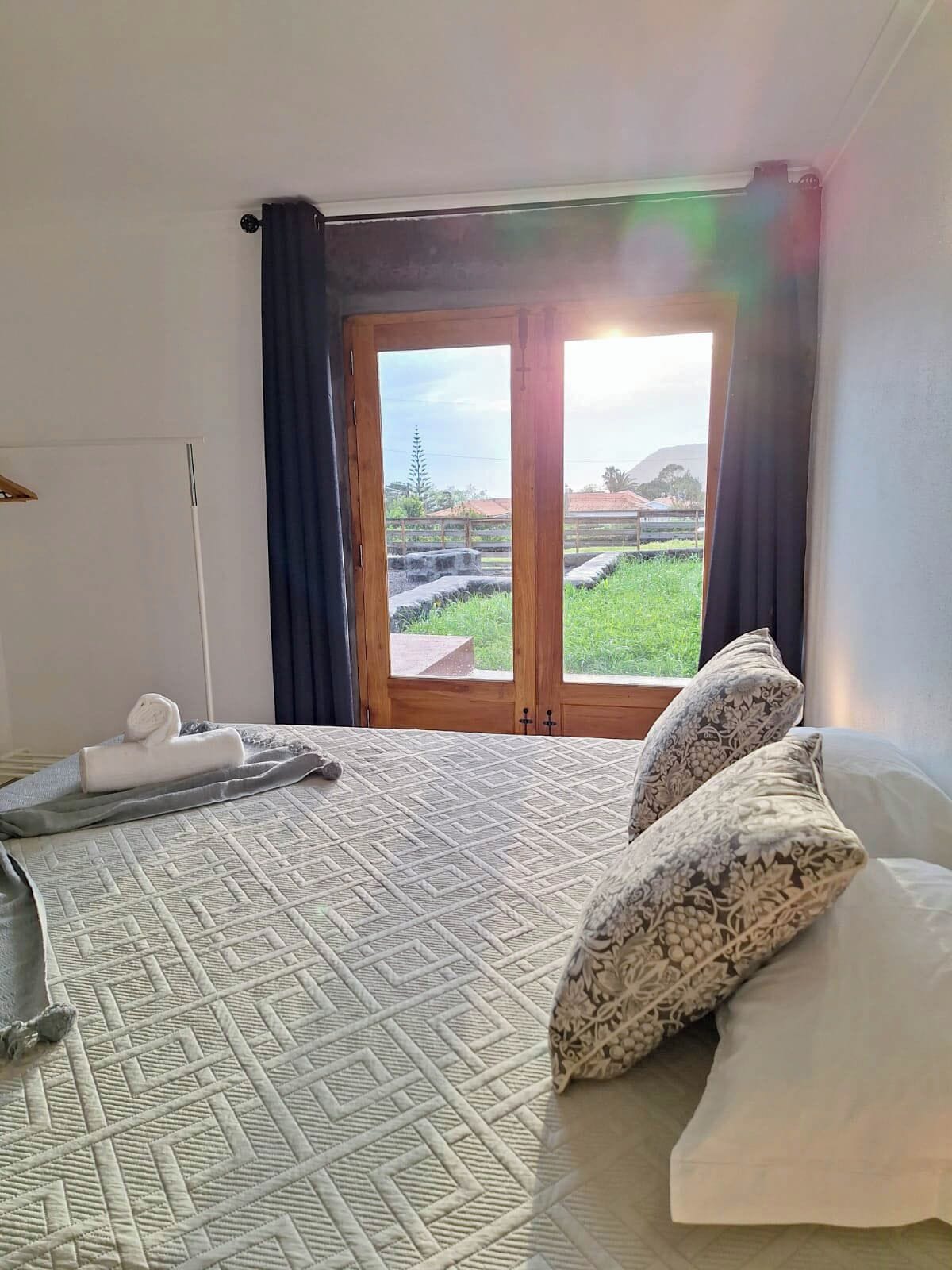 Een hotelkamer met een bed, een handdoek, een kussen en uitzicht op een groen landschap door een raam.