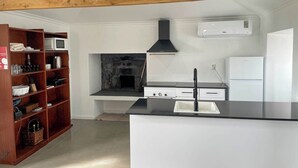 A modern kitchen with a stone fireplace, wooden beams, white cabinetry, and a black countertop.