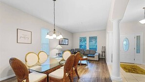 Un comedor con mesa y sillas de madera, un lámpara colgante y un sofá al fondo.