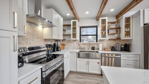 Una cocina moderna con armarios blancos, electrodomésticos de acero inoxidable y vigas de madera en el techo.